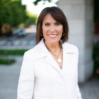 Jennifer McCollum - brown hair, wearing white suite against an outside background