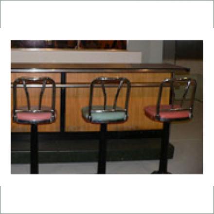 Three stools at a Woolworth’s wooden lunch counter in Greensboro, N.C. From left to right the stools are pink, mint green, and red with metal framed backs. 