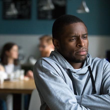 Frustrated excluded outstand african american man suffers from bullying or racial discrimination having no friends sitting alone in cafe