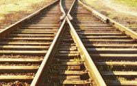 Two railroad tracks merging to become one with golden grass in the background